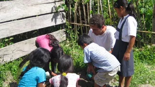 Daniel untersucht mit einer Gruppe von Kindern im Schulgarten die Erde.