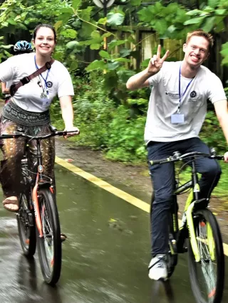 Zwei Menschen fahren Fahrrad und zeigen mit ihren Händen ein Peace Zeichen in die Kamera