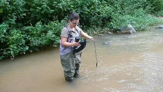 Martina steht in einem Fluss und hält ein Gerät zur Bestimmung der Wasserqualität in der Hand.
