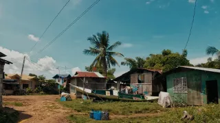 Drei Hütten mit Wellblechdach und ein Boot, im Hintergrund sind Palmen. Die Freiwilligen wohnen in einem Fischerdorf auf der philippinischen Insel Negros.
