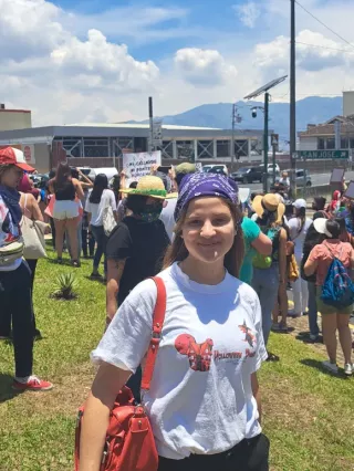 Zum Weltflüchtlingstag am 20. Juni berichtet Antonia von ihrer Freiwlligenarbeit auf Costa Rica. Sie lächelt in die Kamera. Im Hintergrund sind viele Menschen zu sehen.