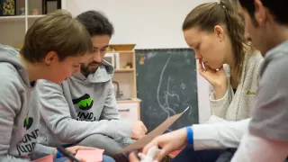 Vier junge Menschen sitzen sich gegenüber und arbeiten zusammen über Papiere gebeugt.