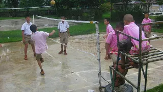 Jungen der 6. Klasse beim Spielen der thailändischen Nationalsportart Takraw. Die Jungen stehen auf zwei Seiten eines Netzes und ein Ball befindet sich in der Luft.
