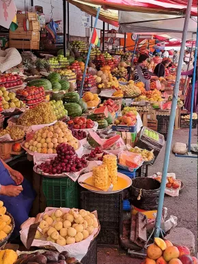 Zu sehen ist ein großer Marktstand mit verschiedenen Früchten und Gemüse, pyramidenähnlich aufeinandergestapelt.