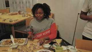 Joseline is sitting at a table decorating biscuits. There are biscuits and decorating materials on the table.