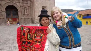 Corinna steht neben einer älteren Peruanerin. Sie hat zwei Fingerpuppen auf den Fingern und die Peruanerin hält ein buntes Tuch in der Hand.
