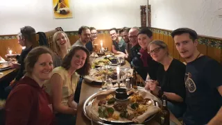Elf junge Menschen sitzen in einem Restaurant an einem langen Tisch und lächeln in die Kamera. Auf dem Tisch stehen Platten mit unterschiedlichen äthiopischen Snacks.