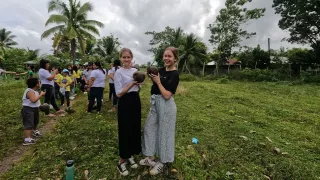 Zwei Frauen stehen auf einem Feld und halten Kokosnuss-Setzlinge in den Händen. Während ihrer Freiwilligenarbeit pflanzen sie Bäume auf der philippinischen Insel.