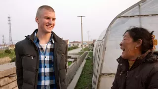 Anton steht neben einer Bäuerin vor einem Gewächshaus. Die beiden lachen und unterhalten sich.