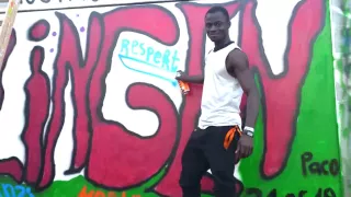 Amani stands in front of a wall with graffiti and smiles at the camera. In his hand, he holds a spray can.