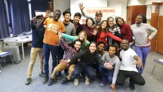 Dieses Foto zeigt Rosario in einer Gruppe junger Menschen in einem Seminarraum. Die jungen Leute strecken ihre Arme aus und sehen fröhlich in die Kamera.
