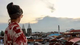 Une volontaire se tient sur un balcon et regarde les toits qui se trouvent devant elle.