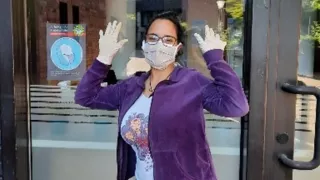 Sofía stands in front of the entrance door of Café International wearing a mask and gloves.