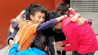 Several boys are standing in a circle with their arms around each other. One of the boys is smiling at the camera.