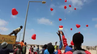 Eine Gruppe Kinder an einer Straße. Sie lassen herzförmige Luftballons in die Luft steigen.