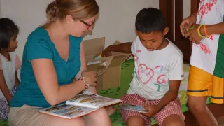 Sarah-Marie liest zwei Kindern eine Geschichte vor. Das eine Kind packt etwas aus einem Karton aus.