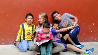 Phoebe is sitting, leaning against a wall. Three boys are sitting around her, looking at the camera, and one boy is on her lap.