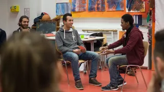 Zwei junge Männer sitzen sich auf Stühlen gegenüber und diskutieren lebhaft.