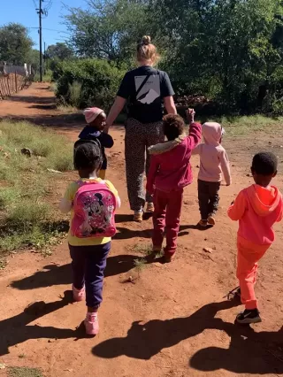 Eine Freiwillige läuft mit Kindern an der Hand. Sie leitet ihre Freiwilligenarbeit in Südafrika.