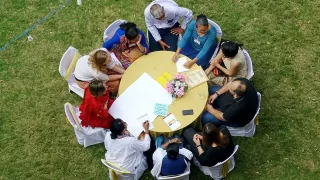 An overhead view of a round table, at which a group is working on some documents together.