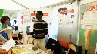 Volunteer Lucky standing at a festival stand, explaining global issues to three bystanders.