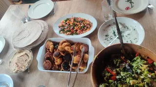 La table du repas est recouverte de vaisselle et de nourriture. On y voit un bol de houmous, un plat à gratin rempli de falafels, une assiette de chapati et un bol de salade de tomates.