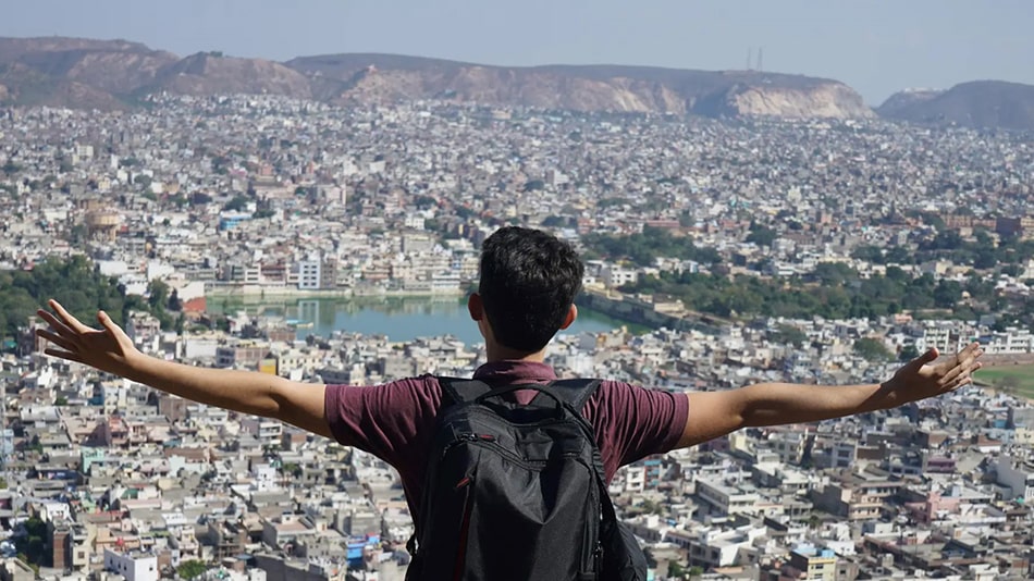 Karim steht mit dem Rücken zur Kamera, hat die Arme weit ausgestreckt und schaut von oben auf eine Stadt.