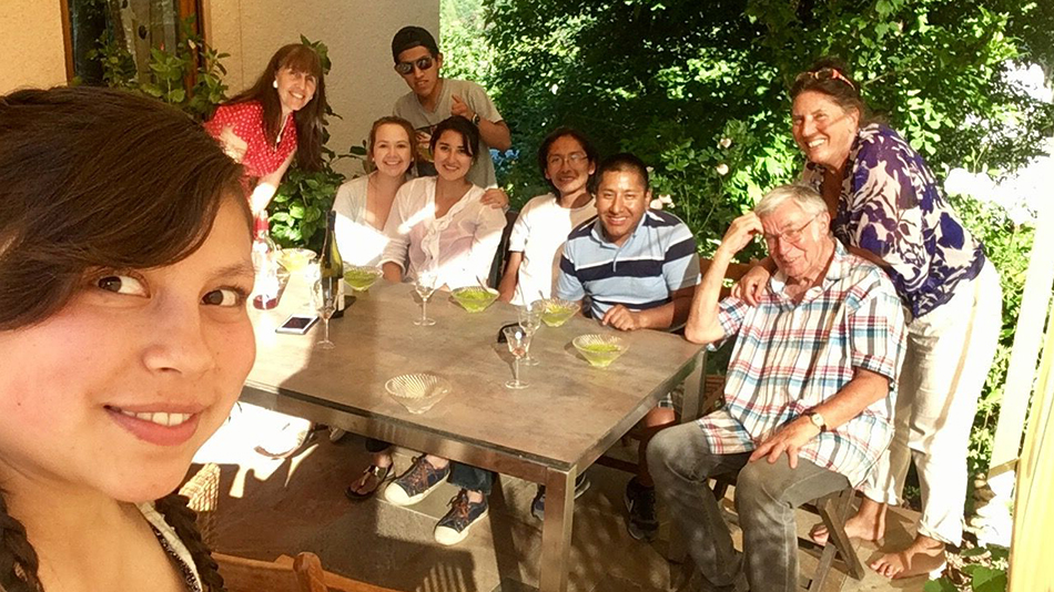 neun Personen sitzen an einem Gartentisch und lächeln für das Selfie in Richtung Kamera