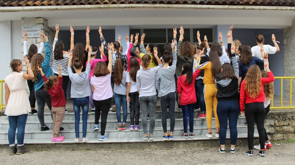 Eine Gruppe von Mädchen ist von hinten zu sehen, sie strecken ihre Hände in die Luft, die mit roter Farbe bemalt sind