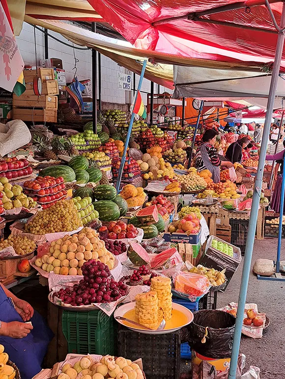 Zu sehen ist ein großer Marktstand mit verschiedenen Früchten und Gemüse, pyramidenähnlich aufeinandergestapelt.