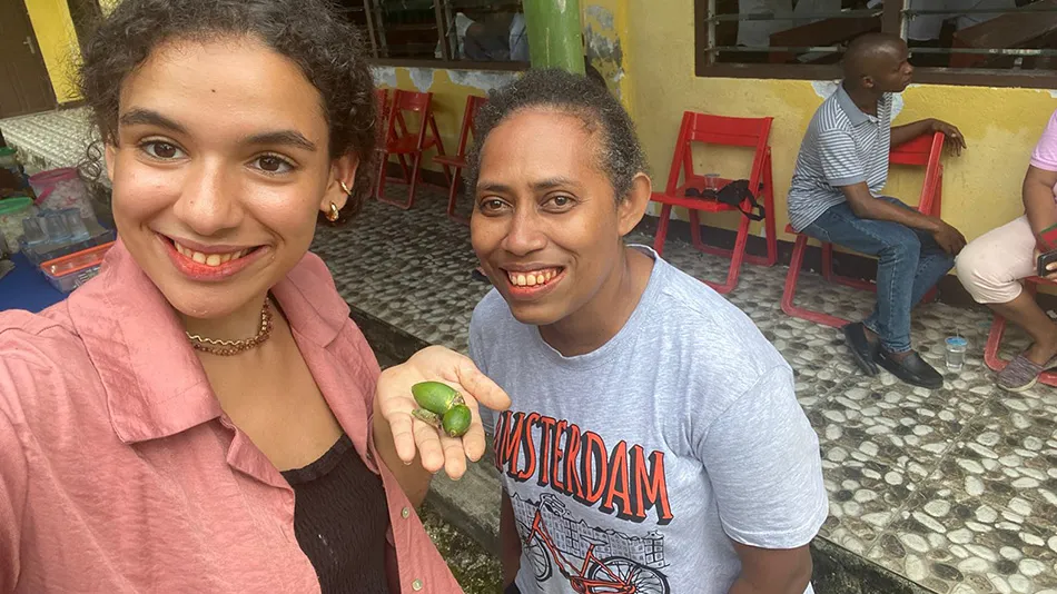 Zwei Frauen lächeln direkt in die Kamera. Die Linke der beiden hält ihre Hand flach hoch, in welcher grüne Früchte liegen.