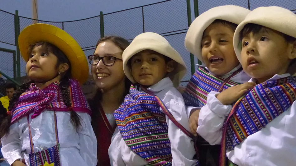 Die Freiwillige steht zwischen peruanischen Kindern, die lokale Kleidung tragen.