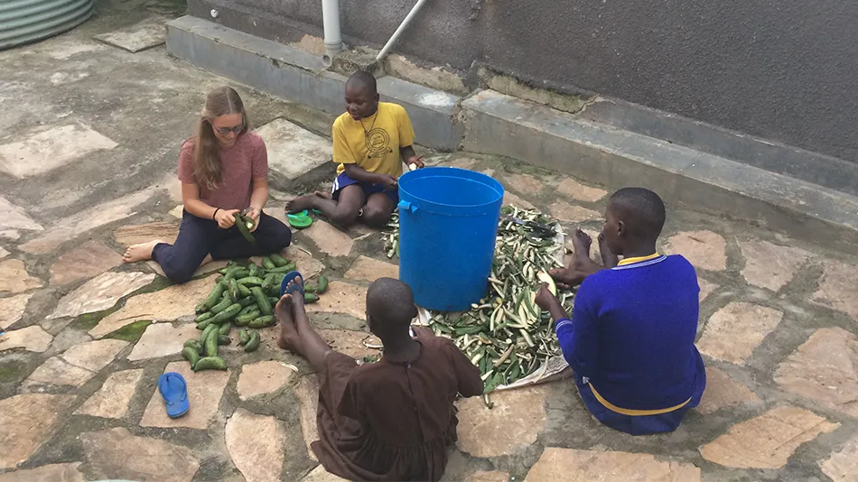Die Freiwillige sitzt mit Kindern auf dem Boden, sie schälen Kochbananen.
