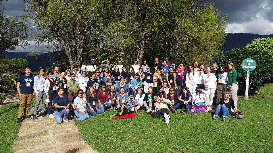 The fifty or so participants of the partner conference pose for a group photo in front of a large tree.